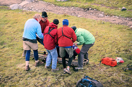 SAR members with help from nearby camper place injured hiker in litter in preparation for transporting to the helicopter